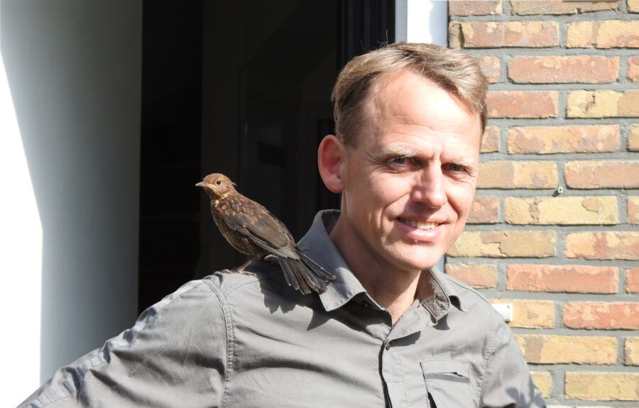 Man met jonge merel op de schouder, beide kijken in de lens.