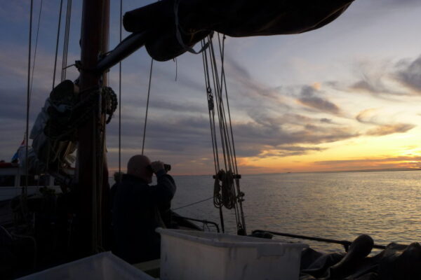 silhouet van een man met verrekijker vanaf een schip. Kijkt over zee bij zonsondergang.