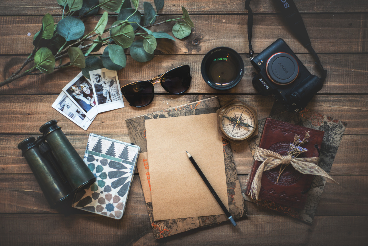 sunglasses, camera, goggles, pen, paper, compass, passport and green leaves on a table