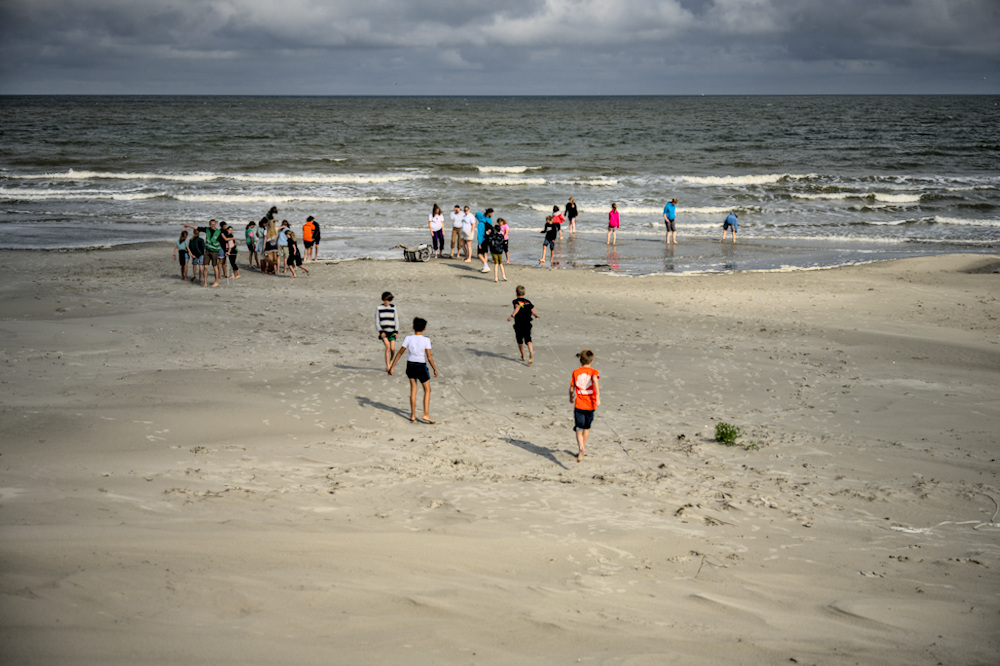 groep kinderen op het strand dicht bij de branding. Enkelen rennen naar de zee toe.