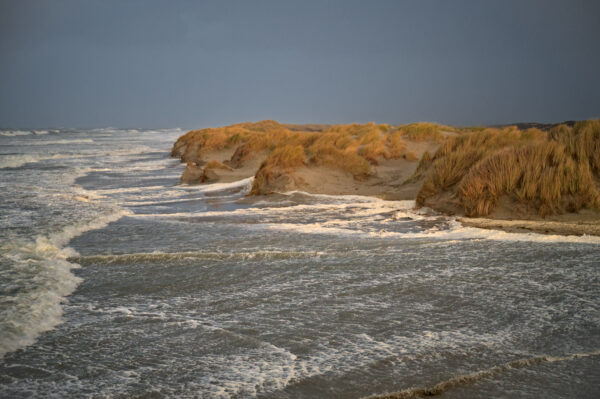 het water van de branding staat hoog op het strand, tot aan de duinen