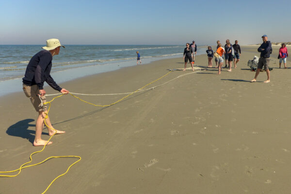 mensen op het strand, iemand trekt aan een touw, verderop ligt een net