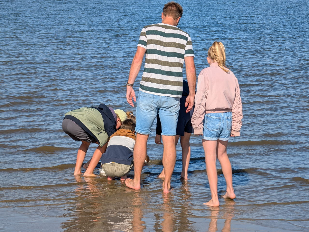 kinderen en een man staan gebogen over iets in zee