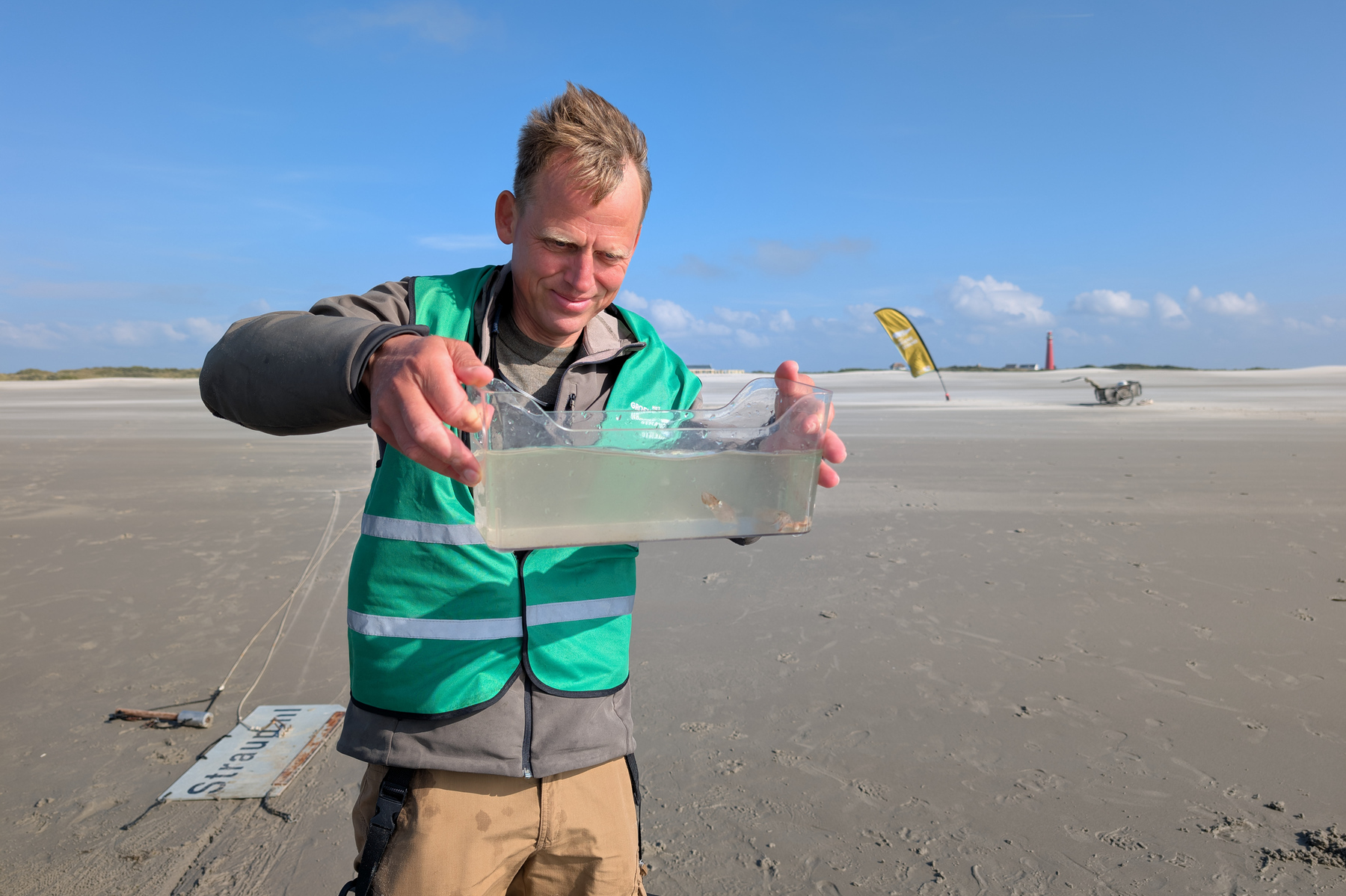 man houdt klein aquarium vast op het strand