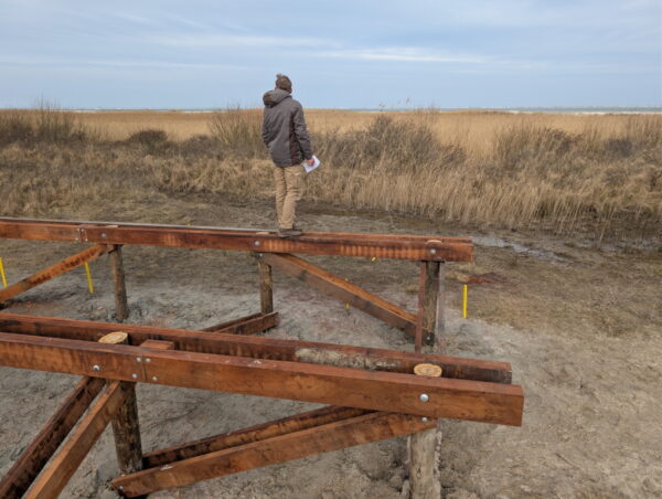 Man staat op houten constructie en kijkt over zee