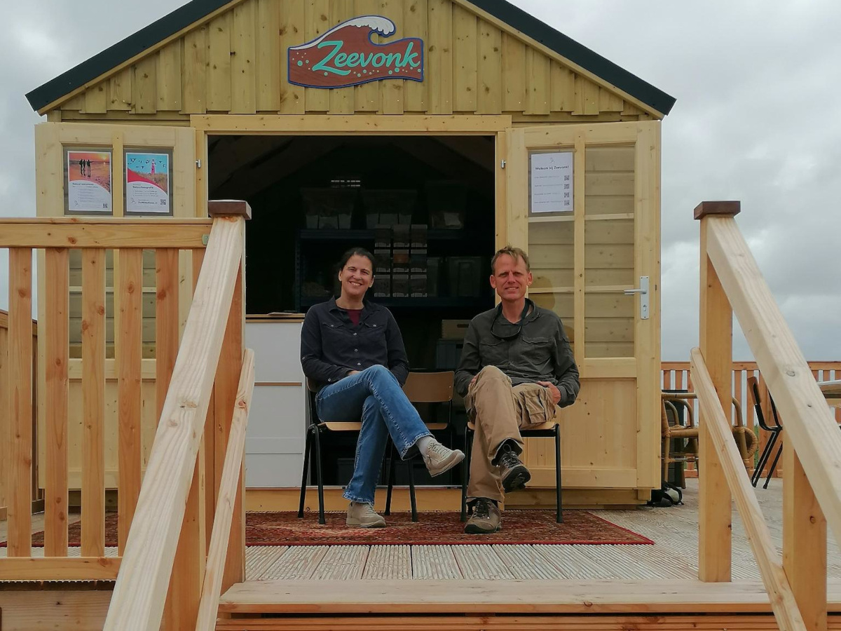 Foto van twee mensen zittend voor een strandhuis met opschrift Zeevonk